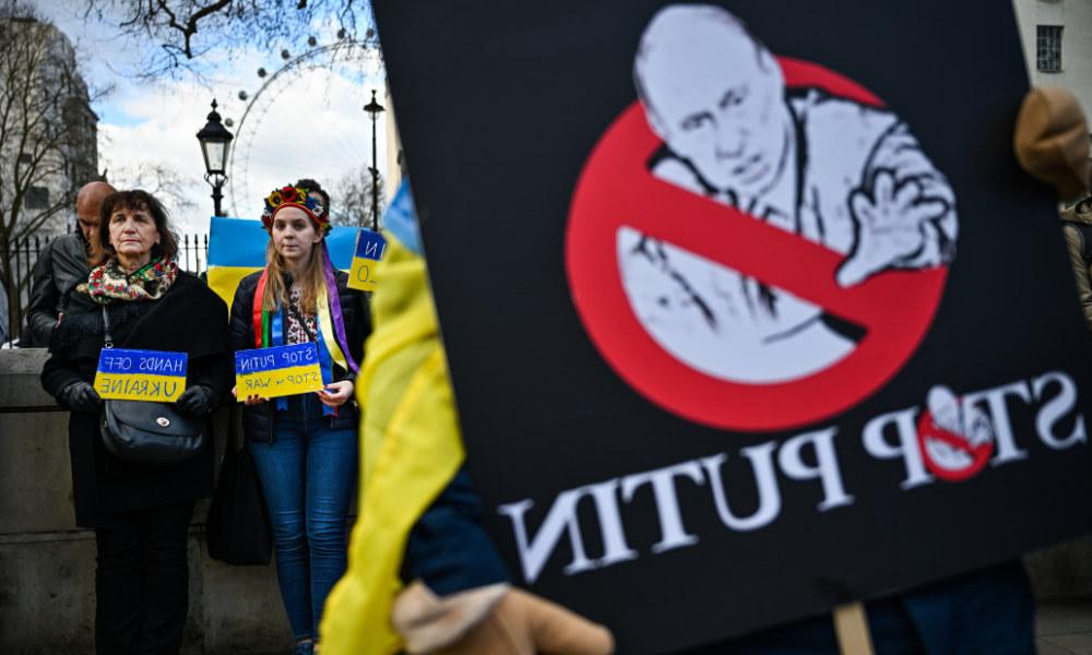 反普京集会标语特写，背景中人们举着带有乌克兰国旗颜色的标语.