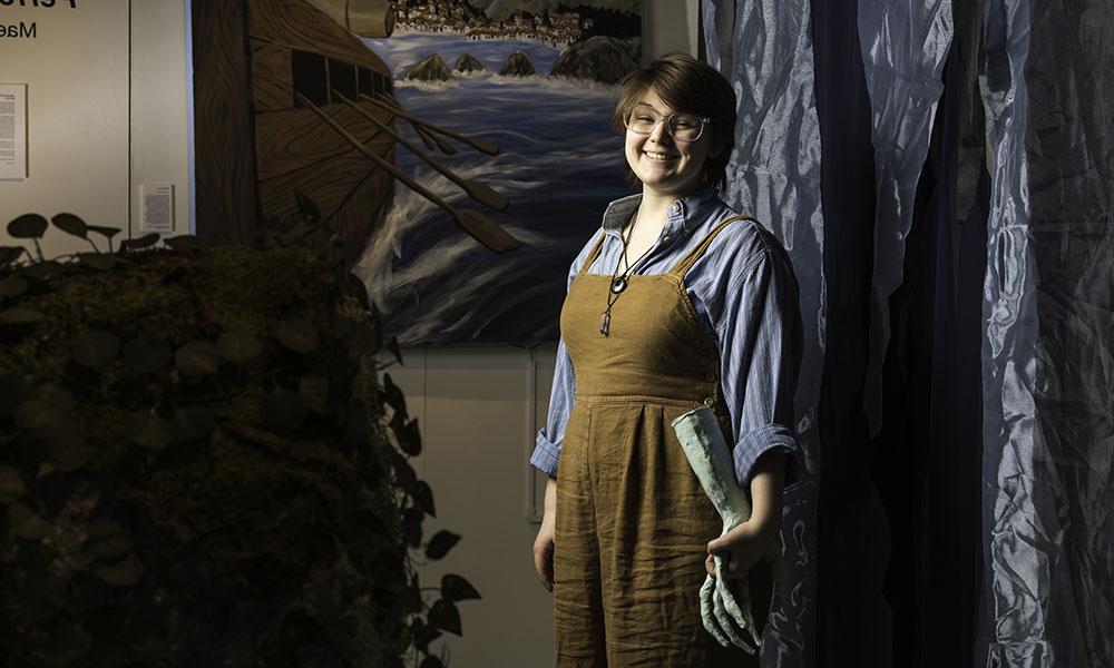 Mae Cooke, from head to knee, smiling in center with painting and sculpture in background.